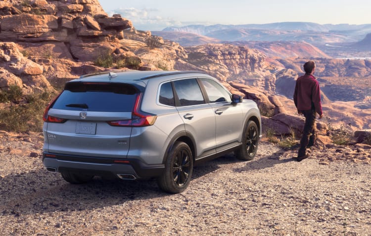 Front passenger-side view of the 2022 Honda CR-V Touring in Radiant Red Metallic with Honda Genuine Accessories, driving in an urban environment.